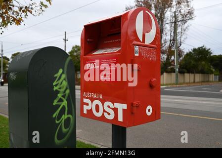 Une boîte postale rouge de l'Australia Post au premier plan, avec une boîte de collecte verte derrière elle, tous deux vandalisés, un jour gris. Banque D'Images