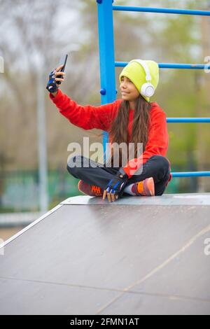 Une fille de dix ans dans un casque blanc prend un selfie sur un smartphone pour l'envoyer à des amis. Autodétermination et concept de culture de la jeunesse. Banque D'Images