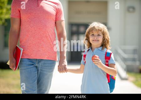 Père et fils américains marchant dans le parc scolaire. Enfant étudiant élémentaire portant des sacs à dos tenant parent père main marchant vers le haut. Banque D'Images