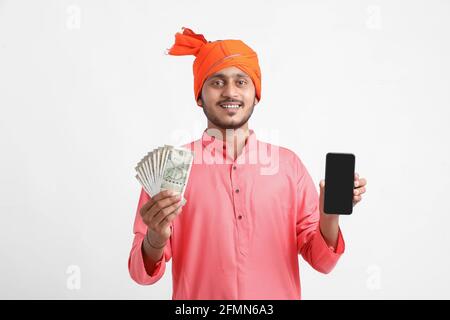 Jeune agriculteur indien utilisant un smartphone et montrant de l'argent sur fond blanc. Banque D'Images