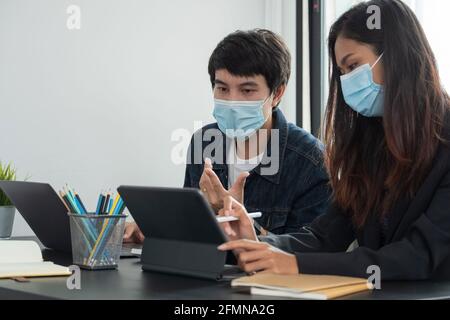 Les hommes d'affaires asiatiques ont une réunion et travaillent au bureau et portent un masque de protection contre le virus corona. Banque D'Images