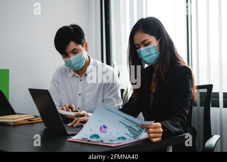 Les hommes d'affaires asiatiques ont une réunion et travaillent au bureau et portent un masque de protection contre le virus corona. Banque D'Images