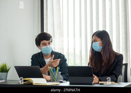 Les hommes d'affaires asiatiques ont une réunion et travaillent au bureau et portent un masque de protection contre le virus corona. Banque D'Images