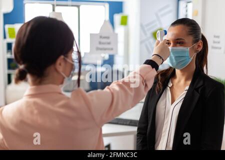 Femme utilisant un thermomètre infrarouge mesurant la température des employés de bureau, lors d'une épidémie mondiale avec coronavirus dans une entreprise commerciale. Nouvelle normale en temps de pandémie mondiale avec covid19. Banque D'Images