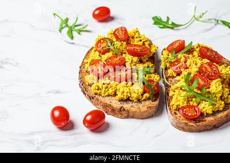 Toasts brouillés au tofu avec tomates et arugula, fond en marbre blanc. Banque D'Images