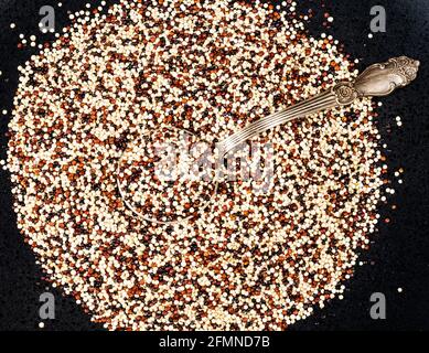 vue du dessus de la cuillère à soupe dans un mélange de graines de quinoa sur plaque noire Banque D'Images