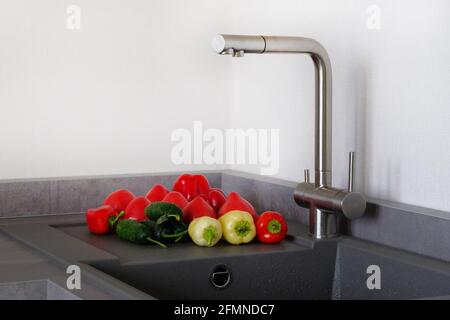 Légumes tomates, concombres, poivrons à côté de l'évier dans la cuisine. Comptoir moderne avec évier dans la cuisine. Concept de lavage des légumes. Banque D'Images