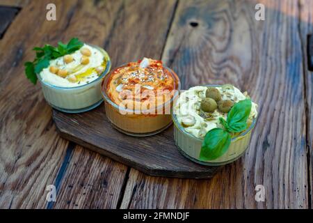 Trois types de houmous classiques avec paprika et ail, olives, pois chiches, tahini, huile d'olive, et épices orientales dans un bol sur une table en bois Banque D'Images