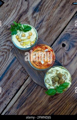 Trois types de houmous classiques avec paprika et ail, olives, pois chiches, tahini, huile d'olive, et épices orientales dans un bol sur une table en bois Banque D'Images