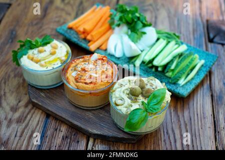 houmous classiques avec paprika et ail, olives, pois chiches, tahini, huile d'olive, et des épices orientales dans un bol sur une table en bois avec des légumes frais Banque D'Images