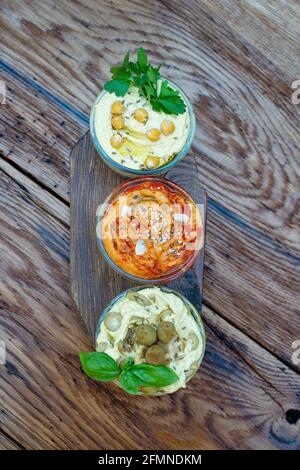 Trois types de houmous classiques avec paprika et ail, olives, pois chiches, tahini, huile d'olive, et épices orientales dans un bol sur une table en bois Banque D'Images