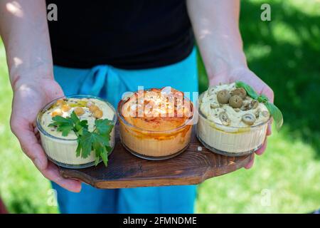 Trois types d'appétissants hummus classiques avec paprika et ail, olives, pois chiches, tahini, huile d'olive et épices orientales dans les mains des femmes. Traditionnel Banque D'Images