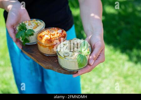 Trois types d'appétissants hummus classiques avec paprika et ail, olives, pois chiches, tahini, huile d'olive et épices orientales dans les mains des femmes. Traditionnel Banque D'Images