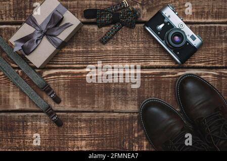 Boîte cadeau pour la fête des pères avec accessoires pour hommes noeud papillon, appareil photo rétro, bretelles et chaussures en cuir sur fond de bois. Copier l'espace. Pose à plat. Banque D'Images