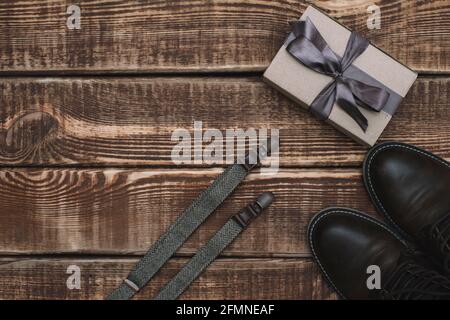Boîte cadeau pour la fête des pères avec accessoires pour hommes, appareil photo rétro, bretelles et chaussures en cuir sur fond de bois. Copier l'espace. Pose à plat. Banque D'Images