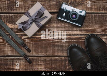 Boîte cadeau pour la fête des pères avec accessoires pour hommes, appareil photo rétro, bretelles et chaussures en cuir sur fond de bois. Copier l'espace. Pose à plat. Banque D'Images