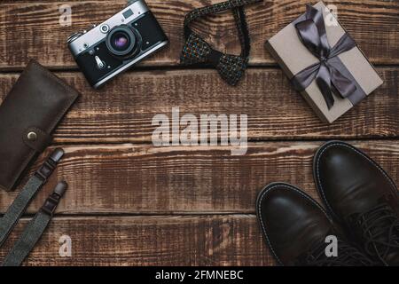 Boîte cadeau pour la fête des pères avec accessoires pour hommes noeud papillon, portefeuille, appareil photo rétro, bretelles et chaussures en cuir sur fond de bois. Copier l'espace. Plat Banque D'Images