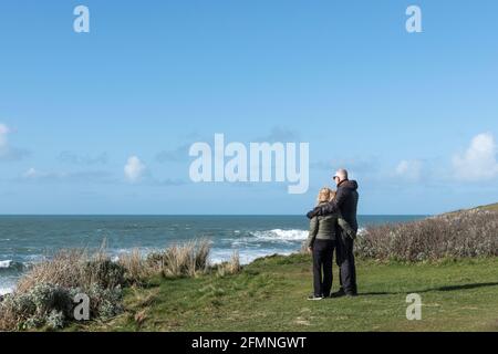 Un couple mature avec des bras l'un autour de l'autre debout sur le promontoire donnant sur la mer à Newquay, dans les Cornouailles. Banque D'Images