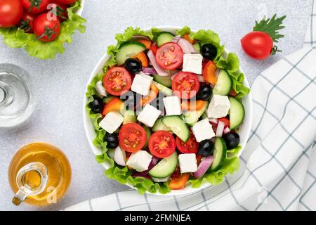 Salade grecque au fromage feta, tomates cerises, concombres, olives et assaisonnées d'huile. Serviette blanche à carreaux sur table grise. Vue de dessus. Une alimentation saine, Banque D'Images