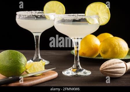 Gros plan de deux verres avec cocktail margarita, sur une table en bois sombre avec des citrons et des limes, fond noir, horizontal Banque D'Images