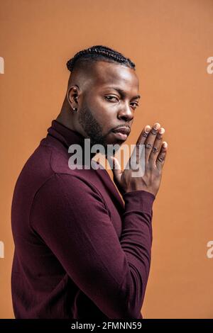 Homme noir aux yeux expressifs regardant l'appareil photo en studio tourné sur fond marron. Banque D'Images