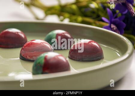 Bonbons au chocolat trempé à la main de collection avec un corps peint brillant sur une plaque ronde avec un fond flou et des éléments bokeh. Stock photog Banque D'Images