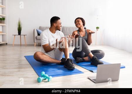 Couple noir regardant des vidéos de sport en ligne sur ordinateur portable, prenant une pause de l'entraînement domestique, parlant entre eux Banque D'Images