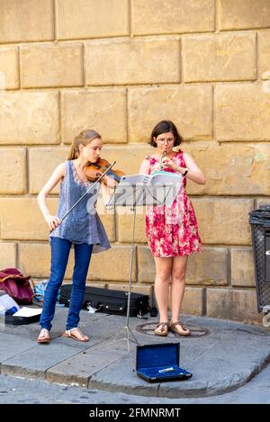 SIENNE, ITALIE - 24 août 2020 : deux jeunes musiciens de rue, l'un avec un violon, l'autre avec un instrument à vent jouant de la musique devant un mur de maison wi Banque D'Images