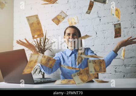 une femme d'affaires joyeuse et prospère qui jette des billets en euros au bureau. chute d'argent Banque D'Images
