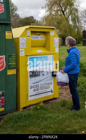 Hampshire, Angleterre, Royaume-Uni. 2021. Femme faisant don de vêtements pour une œuvre de charité en utilisant un conteneur de collecte communautaire pour la charité dans un village du Hampshire. Banque D'Images