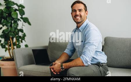 Homme d'affaires confiant sur le canapé dans le hall. Un travailleur indépendant qui a réussi à regarder la caméra et à sourire au bureau. Banque D'Images