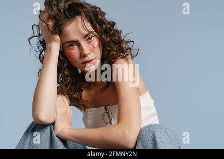 Portrait d'une jolie jeune femme portant un maquillage sous cellules oculaires isolées sur fond bleu Banque D'Images