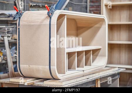 Fabrication de boîtier incurvé de nouvelle armoire en bois avec des étagères à l'aide de attache à bande contemporaine sur banc de travail dans atelier de menuiserie Banque D'Images