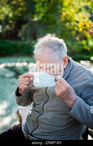 Un homme âgé de 87 ans met un masque tout en étant assis à l'extérieur. Protection contre les virus et les allergènes des personnes âgées. Banque D'Images