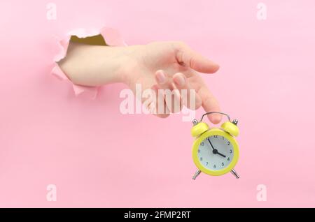 Une main femelle à travers l'arrière-plan tient un réveil rétro jaune. À 15.55 heures, le concept d'une journée de travail de sept heures. Petite montre jaune à l'intérieur Banque D'Images