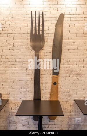 FLORENCE, ITALIE - 24 août 2020 : une table de restaurant devant un mur de briques de couleur sable avec une fourchette et un couteau surdimensionnés fixés au mur pour décembre Banque D'Images
