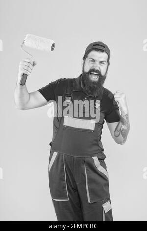 homme brutal heureux en uniforme de boilersuit. mûr hippster utiliser l'outil de rouleau de peinture pour la peinture. réparateur ou constructeur de travail. idée créative. contremaître aller Banque D'Images