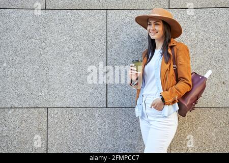 Jolie femme élégante avec sac à dos posant avec une boisson chaude Banque D'Images