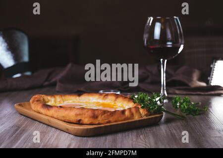 Khachapuri avec des œufs, des herbes et du vin sur la table dans le café. Banque D'Images