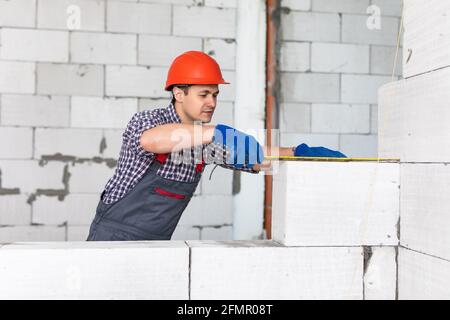 La couche de brique mesure un mur nouvellement construit avec un mètre ruban. Construction Banque D'Images