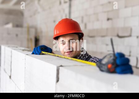 La couche de brique mesure un mur nouvellement construit avec un mètre ruban. Construction Banque D'Images