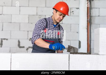 Jeune homme constructeur met sur le ciment de béton cellulaire Banque D'Images