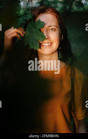Portrait d'une jeune femme souriante avec des feuilles d'érable entre ses mains. Banque D'Images