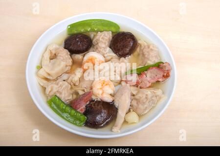 Vue rapprochée depuis le dessus d'un bol en porcelaine blanche rempli de soupe de Wonton sur une table marron clair. Banque D'Images