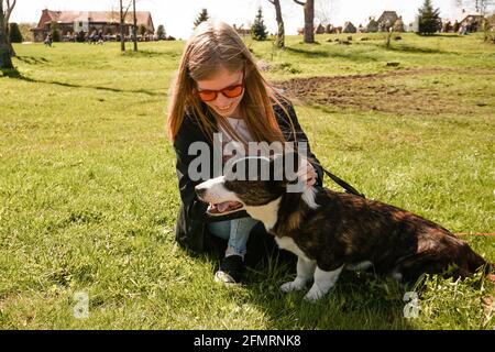 Jeune femme en lunettes de soleil rouges joue avec son corgi sur une pelouse verte d'été. Jour ensoleillé. Un animal de compagnie et un propriétaire heureux Banque D'Images