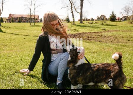 Jeune femme en lunettes de soleil rouges joue avec son corgi sur une pelouse verte d'été. Jour ensoleillé. Un animal de compagnie et un propriétaire heureux Banque D'Images