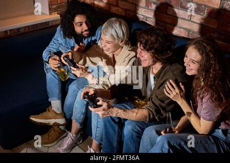 Fou jeunes amis appréciant jouer au jeu vidéo dans la soirée, tenir la compétition pendant le jeu, habillé à la mode Banque D'Images