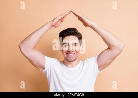 Photo d'une jeune personne insouciante souriant bras montrant la figure de maison isolé sur fond beige Banque D'Images