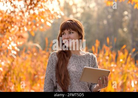 Bonne femme assise utilisant une tablette pendant l'automne marche à l'extérieur stationnement Banque D'Images