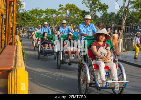 Les pilotes de cyclo chaffent les touristes le long du bord de la rivière dans la vieille ville, Hoi an, Vietnam Banque D'Images